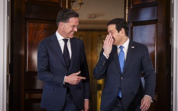 Twee mannen in pak smoezen lachend met elkaar terwijl ze uit een grote deur lopen.