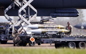 Man staat naast vrachtwagen waarop bommen liggen die onder vliegtuig worden gehangen.