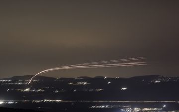 Lichtspoor langs donkere hemel boven heuvellandschap.