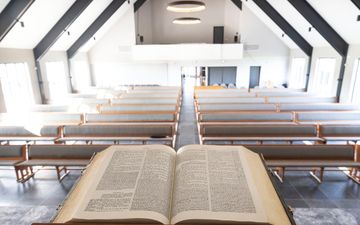 Een opengeslagen kanselbijbel in een nieuwe kerk met een grijze plavuizenvloer en witte wanden. De houten kerkbanken zijn grijs gestoffeerd.