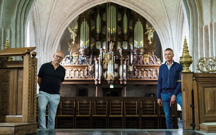 Twee mannen staan in een oude kerk. Achter hen is het front van een oud orgel te zien.