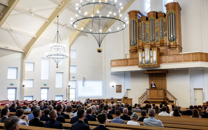 Een kerkzaal vol mensen; op de kansel staat professor Van Vlastuin.