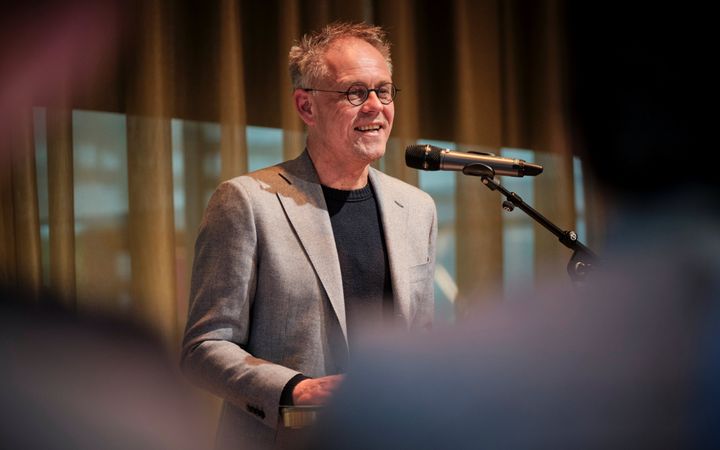 Kees van Ekris, een man met grijs haar, grijs colbert, achter de microfoon.