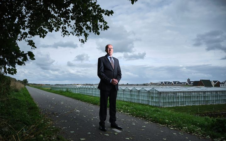 Dominee Tekelenburg, een man in pak, bril op, en op de achtergrond glazen kassen.