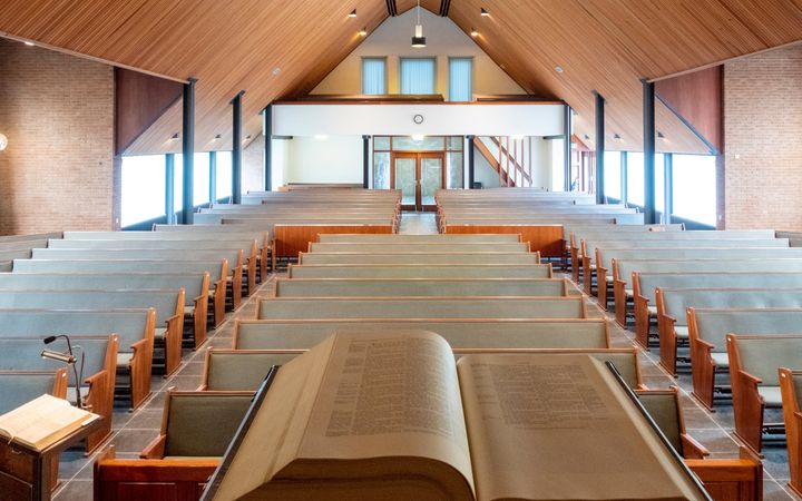 Interieur van kerkgebouw gezien van af kansel met kanselbijbel op voorgrond.