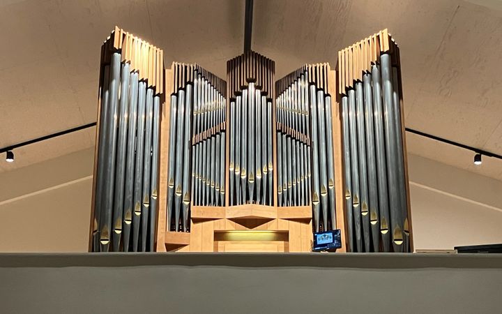 Een orgelfront in een nieuwe kerk met naast de speeltafel een beeldscherm.