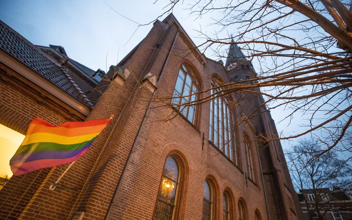 Een regenboogvlag aan de gevel van een oud kerkgebouw.