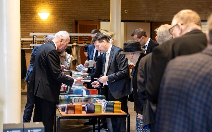 Mensen staan rond een tafel met boeken erop.