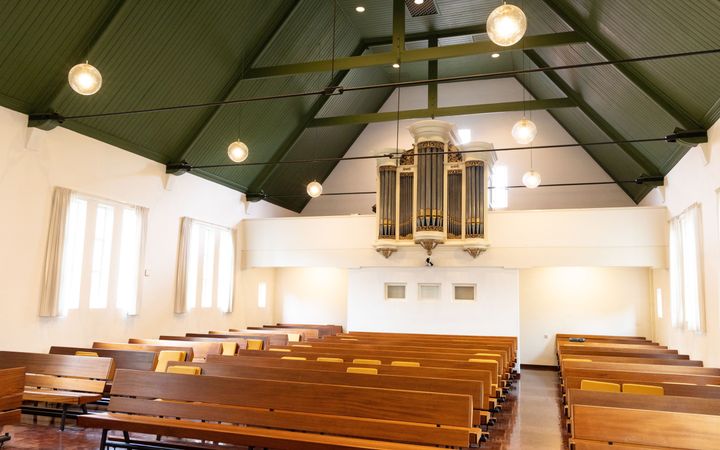 Kerkzaal met houten banken en een orgel.