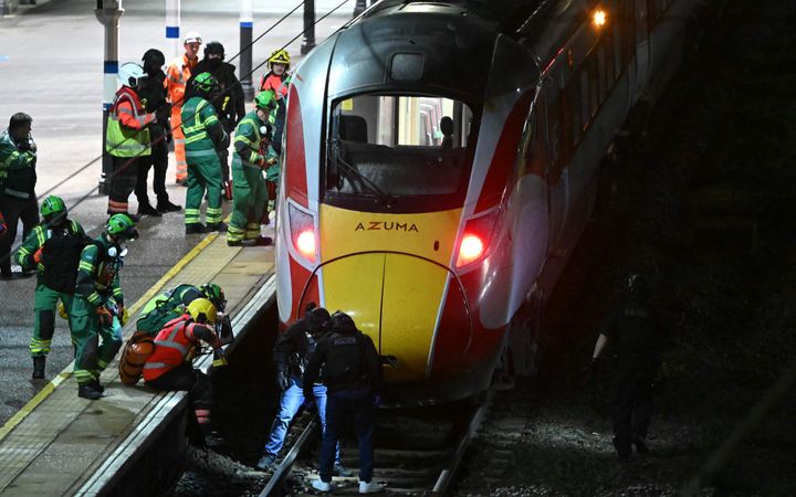 Mannen in groene en oranje reflecterende kleding staan op het perron naast een geel-rode trein.