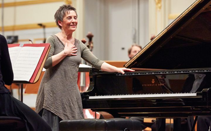 Een pianist staat op een podium naast een vleugel, met een hand op het instrument