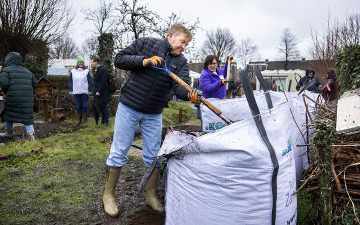Koning Willem-Alexander schept grond uit een bigbag. 