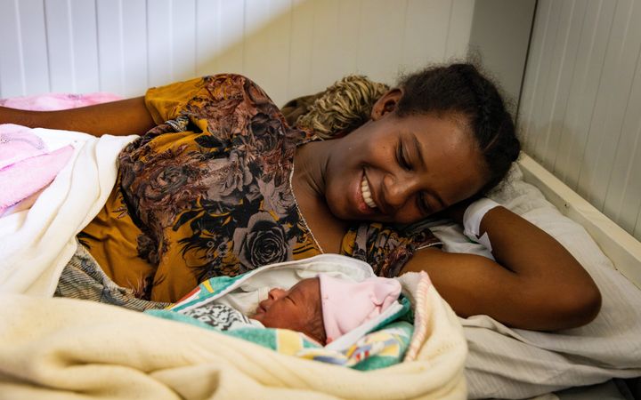 Jonge moeder kijkt glimlachend naar haar pasgeboren jongetje, dat ligt met zijn oogjes dicht naast haar in bed.