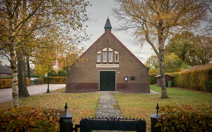 Een klein gebouwtje met gras eromheen, links een parkeerplaats. Op de voorgrond een hekje voor een pad dat naar de ingang leidt.
