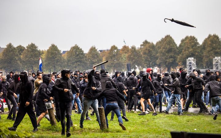 Mannen in donkere kleding rennen over het gras en gooien spullen.