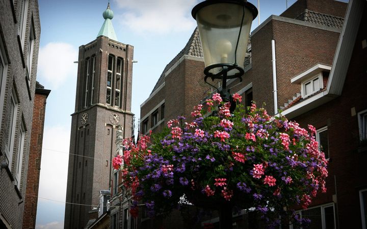 Een kerktoren achter een bloembak met paarse en roze bloemen aan een lantaarnpaal