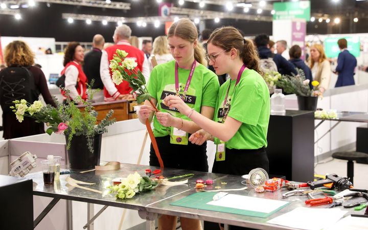Twee meiden in een groen shirt maken een bosje bloemen. 