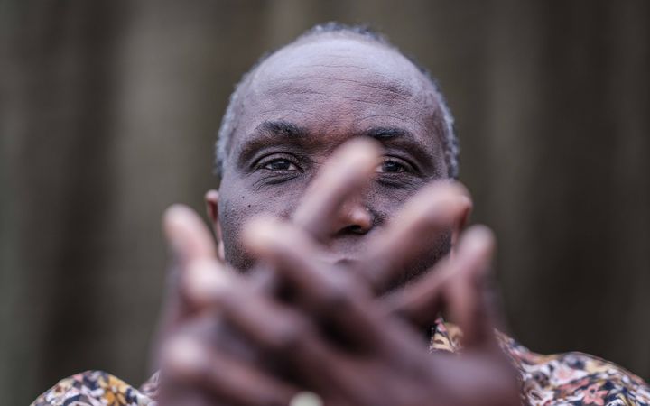 Man met donkere huid, verbergt zijn gezicht achter zijn handen. 