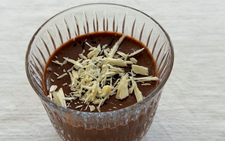 In een glas zit chocolademousse. Erop schilfers witte chocolade.