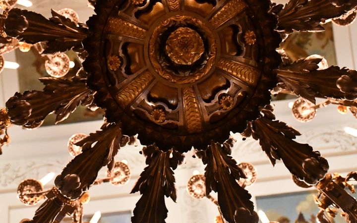 Fraai bewerkte kroonluchter tegen een plafond. Je kijkt er van de onderkant tegenaan.