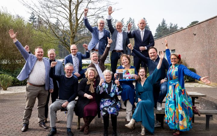 Groepsfoto met juichende mannen en vrouwen. In het midden vrouw met een cheque met het eindberag van de actie. 