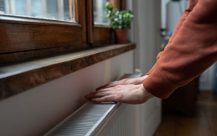 Close-up van een man in een trui die zijn handen op de verwarming legt om zich op te warmen.