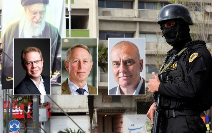 Een grote banner met drie Iraanse leiders, met baarden. In de buurt loopt een  in zwart gehulde, zwaarbewapende man. 