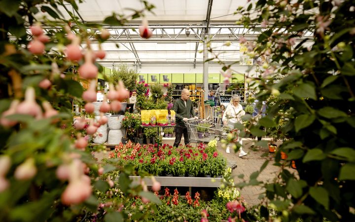 Een oudere man en een vrouw lopen met een winkelwagentje tussen planten in een tuincentrum.