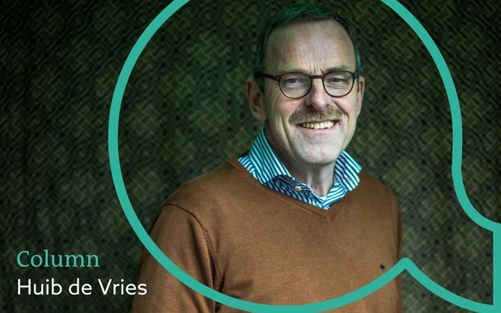 Vignet met daarop een foto van een lachende man met bril en snor. Hij draagt een bruine trui met daaronder een gestreept overhemd. Om de foto heen een groene open komma.
