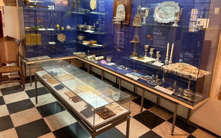 Een vitrine met zilverwerk, oude boeken, kaarsen en andere voorwerpen.