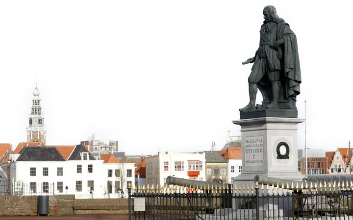Stadsgezicht met huizen en kerktoren. Op de voorgrond staat een bronzen standbeeld van een man in zeventiende-eeuwse kleding.