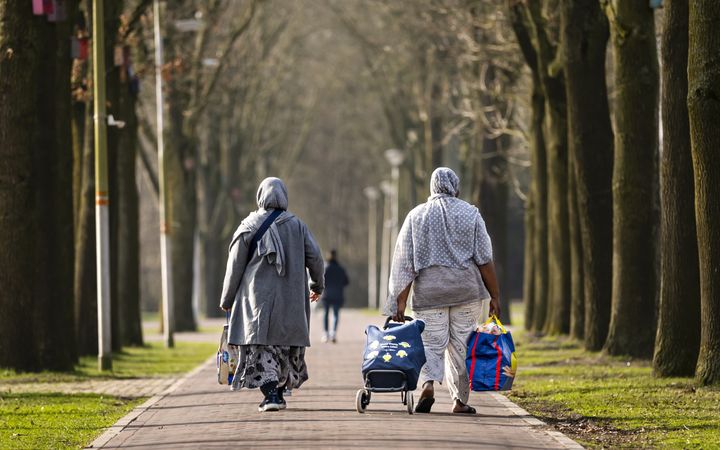 Twee mensen met hoofdbedekking dragen tassen en wandelen over een pad