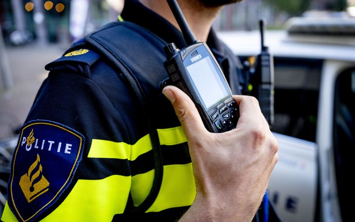 Een hand houdt een portofoon vast, met daarachter een blauw-wit politieuniform