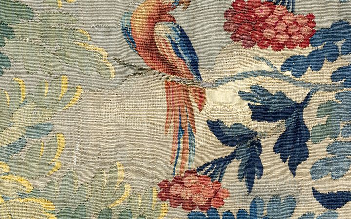 Detail van een wandtapijt met een kleurige vogel op een tak met blauwe bladeren en rode bessen.
