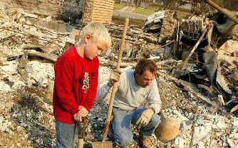 SAN BERNADINO â€“ Marty Bratecher en zijn 8 jarige zoon Mason zoeken verslagen naar waardevolle spullen op de puinhoop van wat hun huis was. Bosbranden in het zuiden van CaliforniÃ« hebben al aan 13 mensen het leven gekost en meer dan 800 huizen in de as 