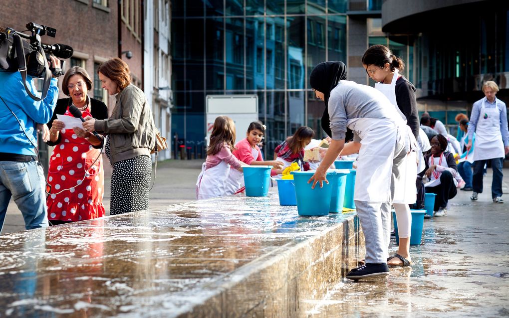 Een schoolklas maakt de Grondwetbank schoon voor het gebouw van de Tweede Kamer in Den Haag. Op de bank staat de tekst van artikel 1 van de Grondwet geschreven. Archiefbeeld ANP, DAVID VAN DAM