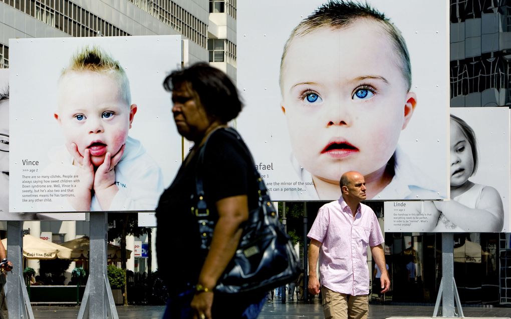 Voorbijgangers lopen op het Spuiplein in Den Haag langs portretfoto's van kinderen met het downsyndroom. beeld ANP, Ed Oudenaarden