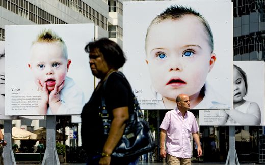 Voorbijgangers lopen op het Spuiplein in Den Haag langs portretfoto's van kinderen met het downsyndroom. beeld ANP, Ed Oudenaarden