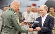 De Duitse bondskanselier Olaf Scholz ontvangt een miniatuur van een militair vliegtuig tijdens een NAVO-oefening. De Duitse regering maakte woensdag bekend aan de NAVO-norm van 2 procent te voldoen. beeld AFP, Axel Heimken