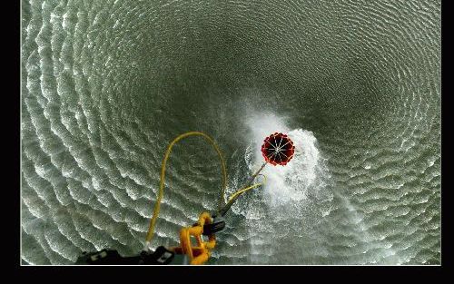 De ”bambi bucket”, een flexibele watercontainer die veel weg heeft van een grote parachute, hangt aan een staalkabel onder de Chinook helikopter. Met een druk op de knop gaat de bucket open en valt er bijna 10.000 liter slootwater uit. De golven in het wa