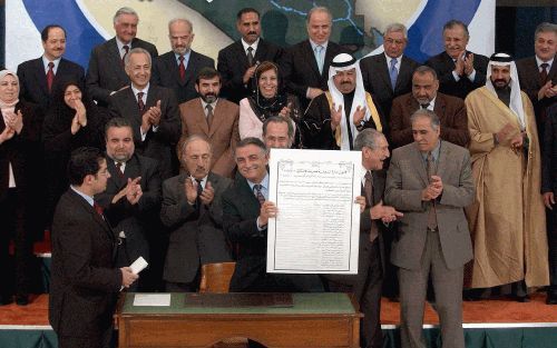 BAGDAD â€“ Een lid van de Iraakse regeringsraad houdt een exemplaar van de interim grondwet omhoog, na de ondertekening van het document afgelopen maandag. Foto EPA