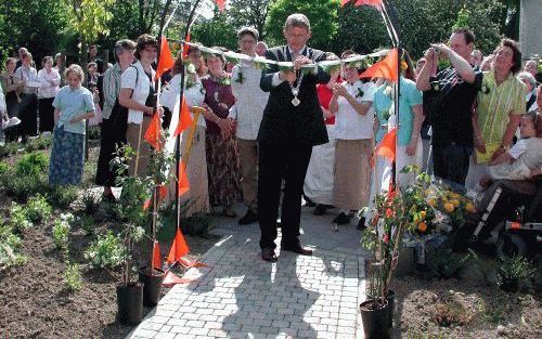 THOLEN â€“ Gadegeslagen door bewoners, personeel en andere belangstellenden knipt burgemeester W. Nuis van Tholen een lint door op het toegangspad naar de nieuwe woonlocatie De Klimroos van zorginstelling Siloah. Foto Eendrachtbode