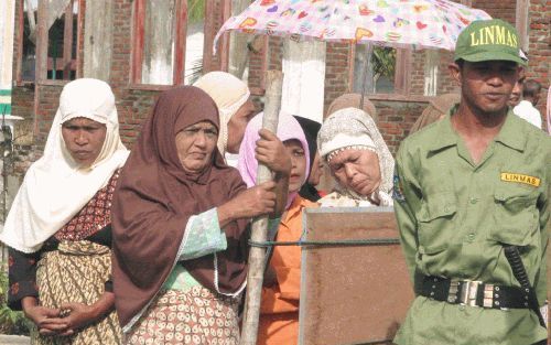 UJUNG PANCU - Een Indonesische veiligheidsagent houdt de wacht bij een stembureau in de provincie Atjeh waar enkele vrouwen in de rij staan om hun stem uit te brengen. De bevolking van het grootste moslimland koos maandag een nieuwe president. Foto EPA