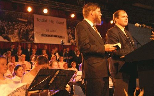 BARNEVELD - De Russische evangelist Andrej Joedintsev (rechts), ooit de jongste geloofsgevangene in Rusland, was een van de sprekers op de jubileumdag van Friedensstimme in Barneveld. Hij werd vertaald door Arie Pellegrom. Achter hen het koor en orkest va