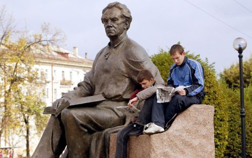 KIEV â€“ Jonge OekraÃ¯ners lezen de krant in Kiev bij een beeld van de dichter Maxim Rylskiy. Foto EPA