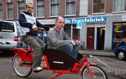 AMSTERDAM â€“ Yalcin Cihangir bestuurt model ”995” van De Fietsfabriek. In de bak zit zijn compagnon, Dave Deutsch. Samen ontwerpen, produceren en verkopen ze fietsen. Volgens techneut Yalcin vraagt de klant sterke fietsen. „Onze fietsen moeten sterk zijn