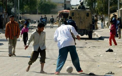 BASRA â€“ Kinderen voetballen op straat in de Zuid Iraakse stad Basra. Op de achtergrond rijdt een Brits legervoertuig. In heel Irak wordt uitgekeken naar de uitslagen van de verkiezingen van afgelopen zondag. Uit de 3,3 miljoen stemmen die tot vrijdag wa