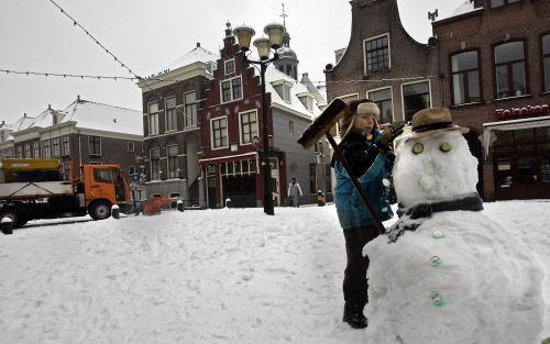 ALKMAAR â€“ Een jongetje maakt een enorme sneeuwpop in het centrum van Alkmaar. Op de achtergrond probeert een sneeuwruimer de straat schoon te maken. Foto ANP