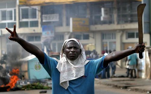 LOMÃ‰ â€“ Een aanhanger van de Togolese oppositie maakt met zijn rechterhand het V teken terwijl hij met zijn linkerhand een kapmes vasthoudt. In de Togolese hoofdstad LomÃ© braken dinsdag rellen uit nadat bekend was geworden dat Faure GnassingbÃ© tot win