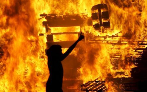 BELFAST â€“ Een Noord Ierse protestant uit zijn vreugde bij een vuur dat op Newtownards Road, in het oosten van Belfast, is aangestoken. Foto EPA